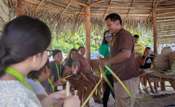 A Department of Community and Cultural Affairs (DCCA) staff member teaches Rota campers and counselors how to weave basic accessories.